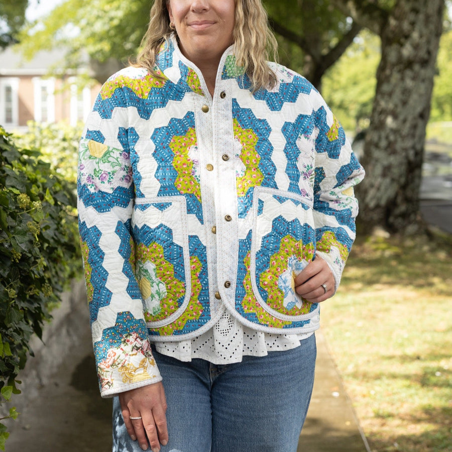 Woman wearing a colorful patterned jacket standing outdoors in a park-like setting.