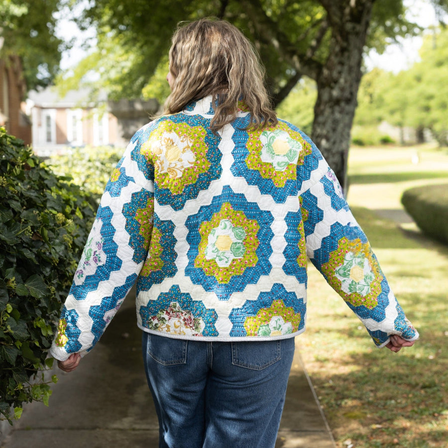 Person wearing a colorful geometric-patterned jacket walking outdoors on a sunny day.